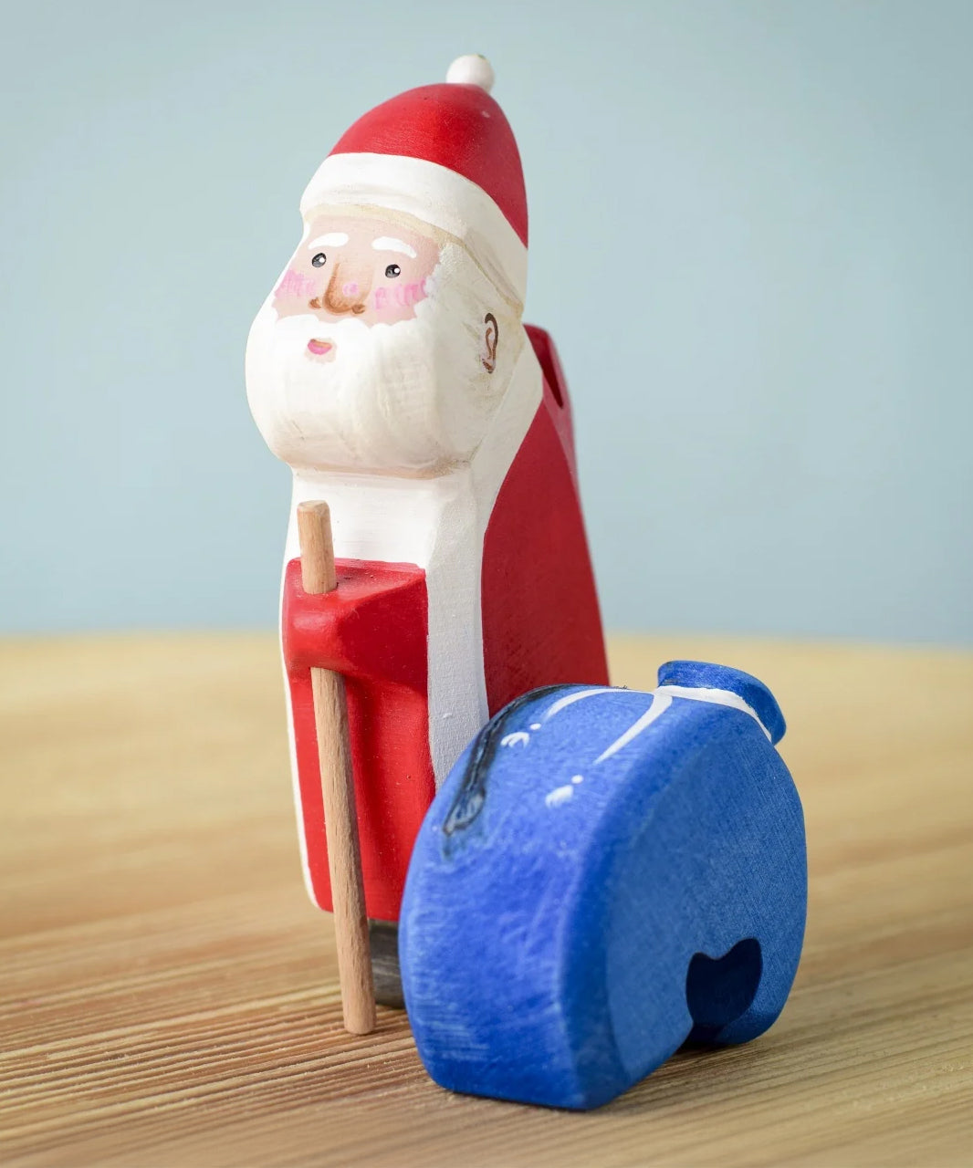 Santa has put down the blue sack with the image showing Santa holding onto a wooden stick with the blue wooden sack next to the figure