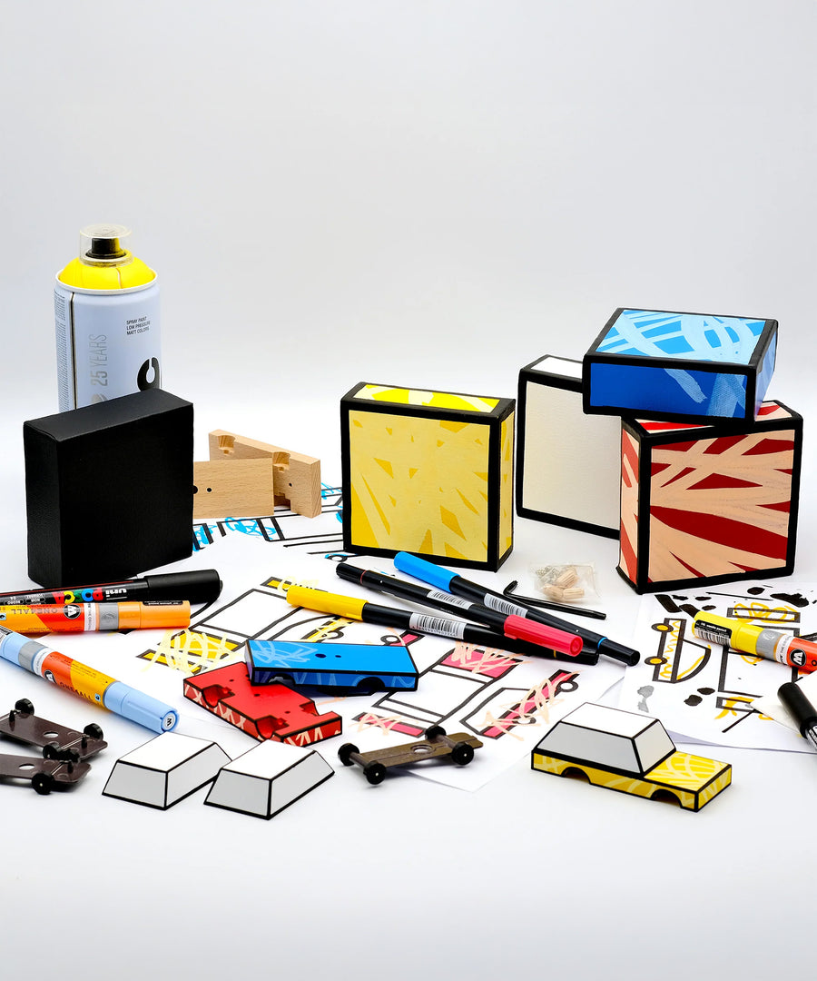 A colourful car construction scene, with coloured boxes, car parts, pens, markers, and a spray can laid out on a light grey background