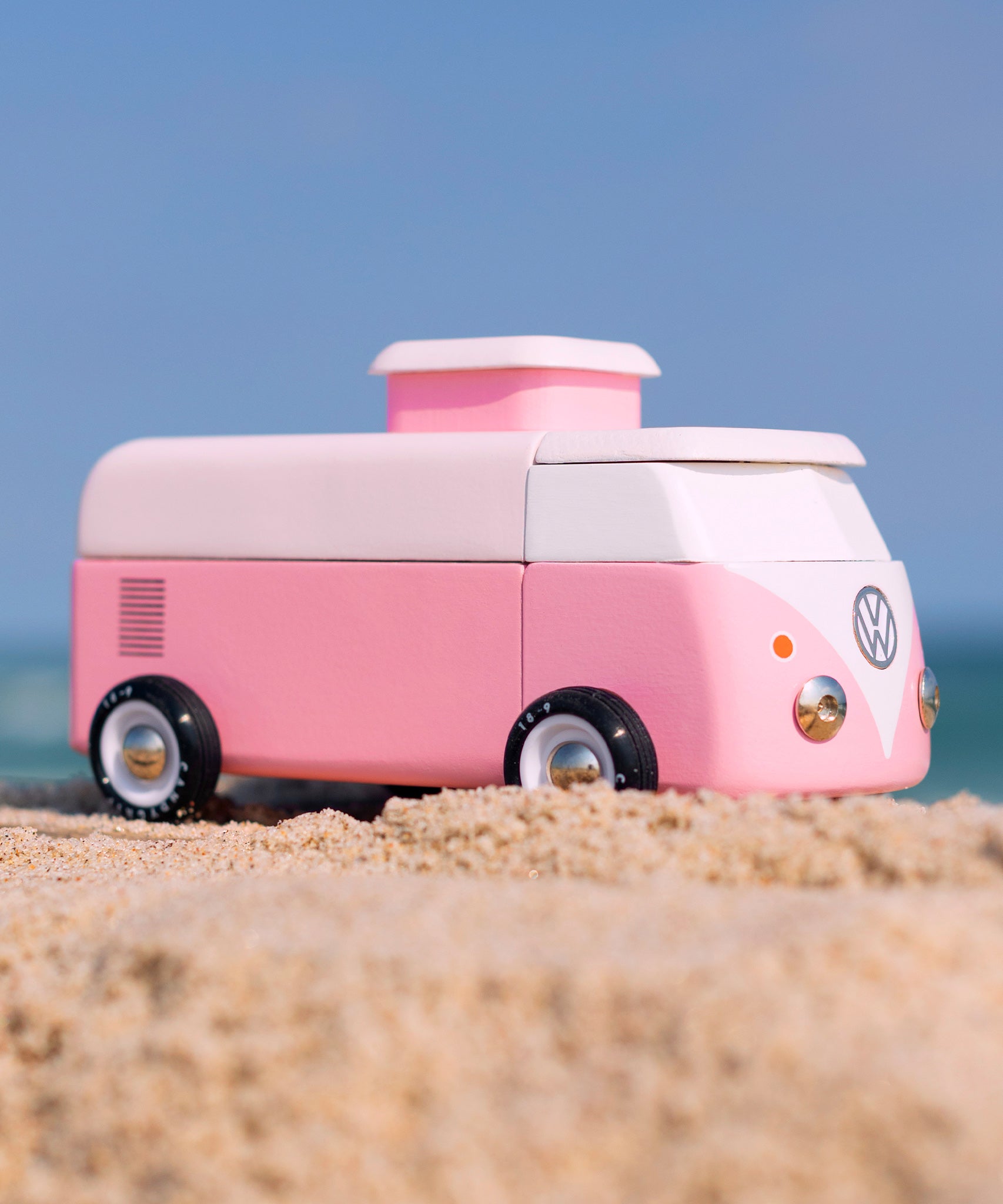 Candylab VW Beach bus in pink, stood on a sandy beach with a blue sky background