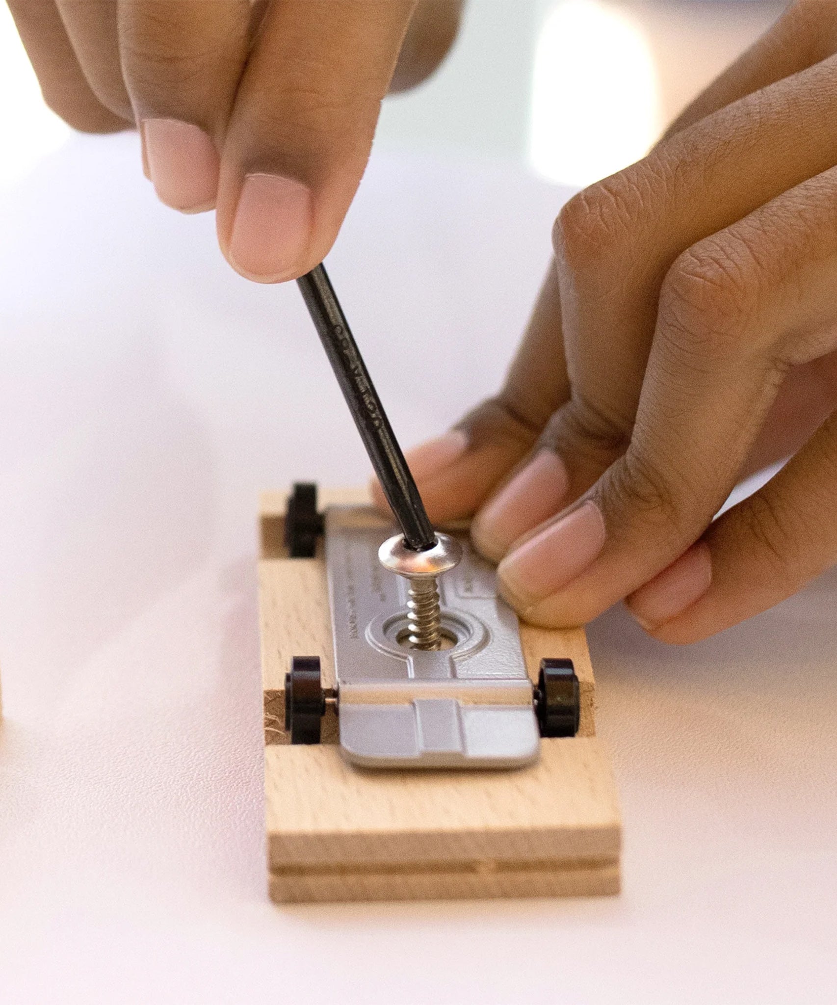 A person putting a screw and metal base into a Candycar wooden block, to make their own toy vehicle. The person is using a black alan key to turn the screw