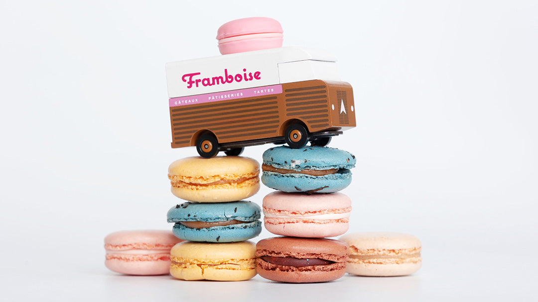 A Candylab wooden toy macaron van on top of colourful macarons