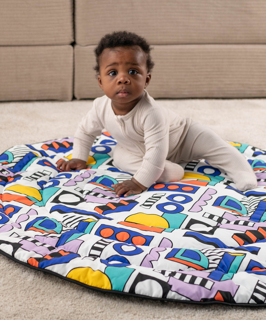 A child happily sat on the Etta Loves x Camille Walala Reversible Playmat, exploring the colourful shape print