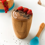 A chocolate pudding with fresh raspberries and chocolate chips, in a bamboo baby cup with blue silicone and bamboo baby spoon.