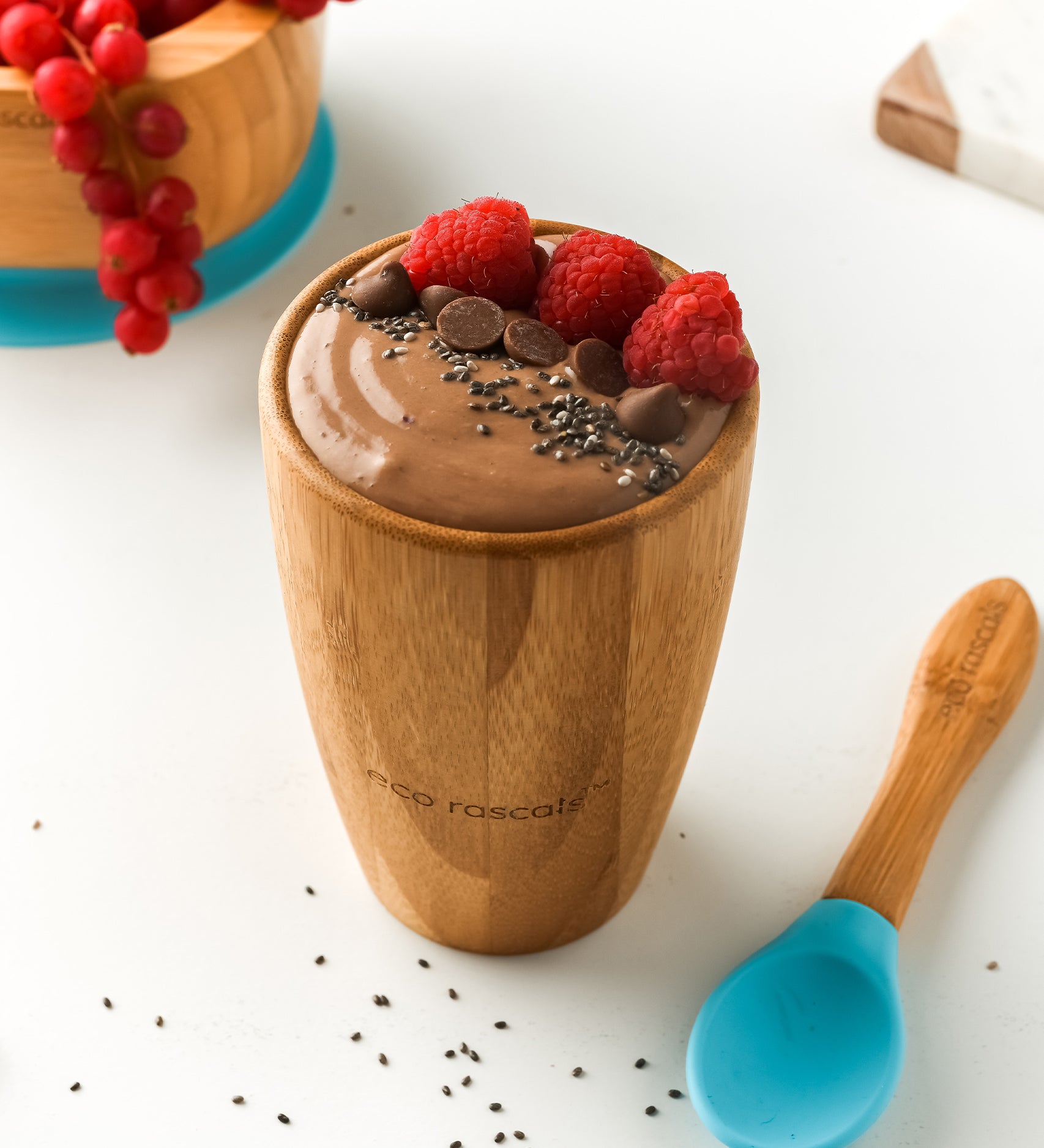 A chocolate pudding with fresh raspberries and chocolate chips, in a bamboo baby cup with blue silicone and bamboo baby spoon.