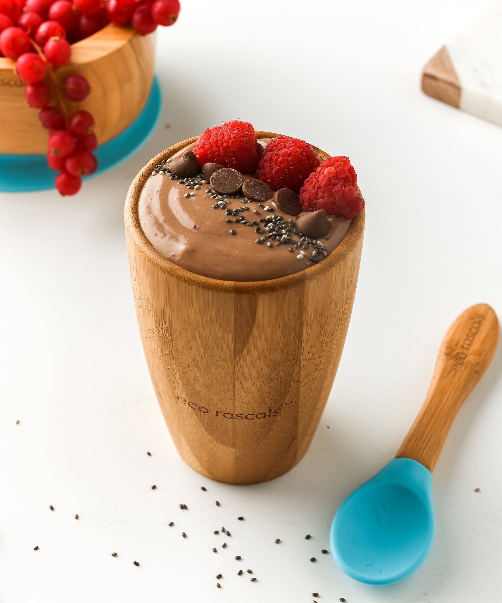 A chocolate pudding with fresh raspberries and chocolate chips, in a bamboo baby cup with blue silicone and bamboo baby spoon.