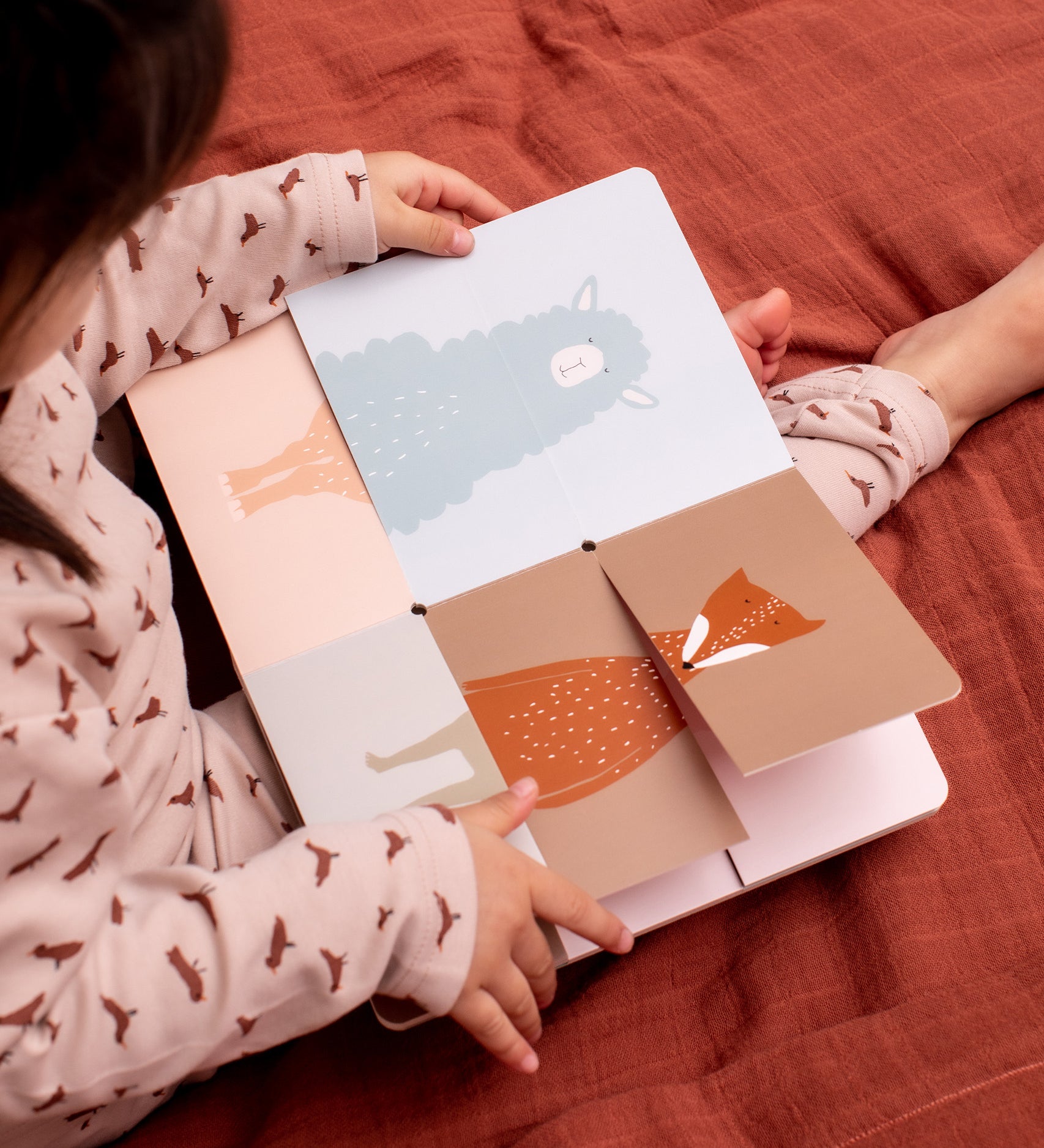 Child sat on a red blanket looking at the Trixie Flip-Flap Animals Book