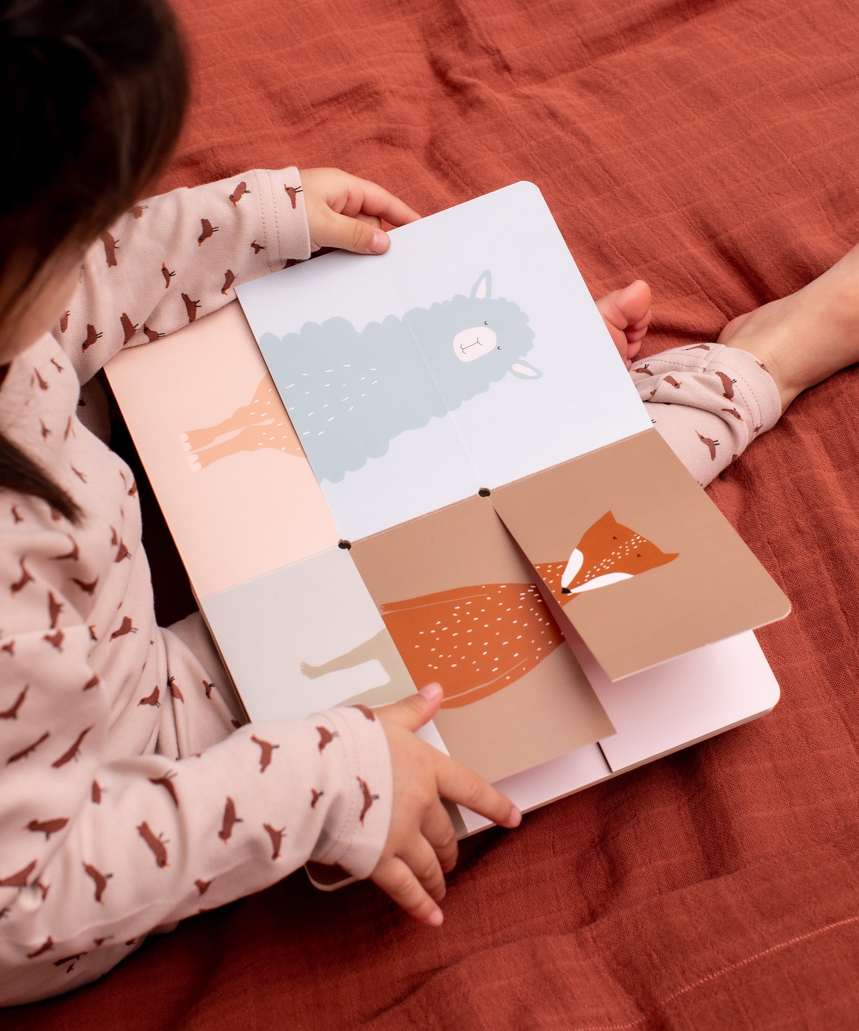 Child sat on a red blanket looking at the Trixie Flip-Flap Animals Book