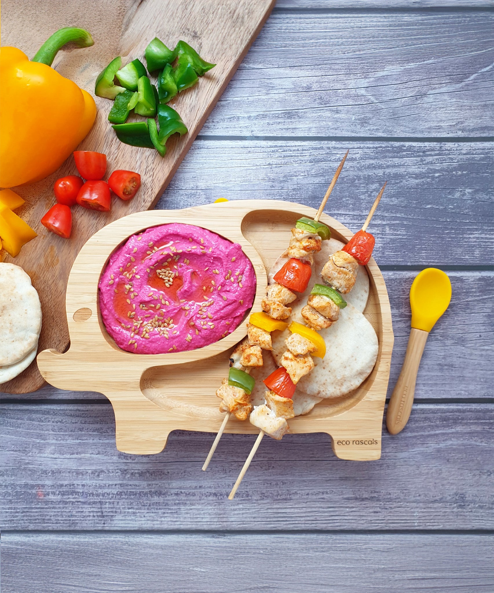 Elephant bamboo baby weaning plate with chicken and vegetable kababs, a pink dip and mini flatbreads,  with a yellow silicone and bamboo baby spoon.