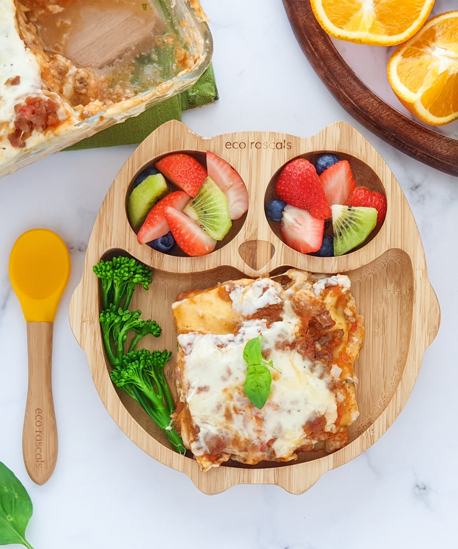 Eco Rascals Owl Bamboo Suction Plate with lasagna, broccoli and two portions of fruit salad, with and orange silicone and bamboo baby spoon. 