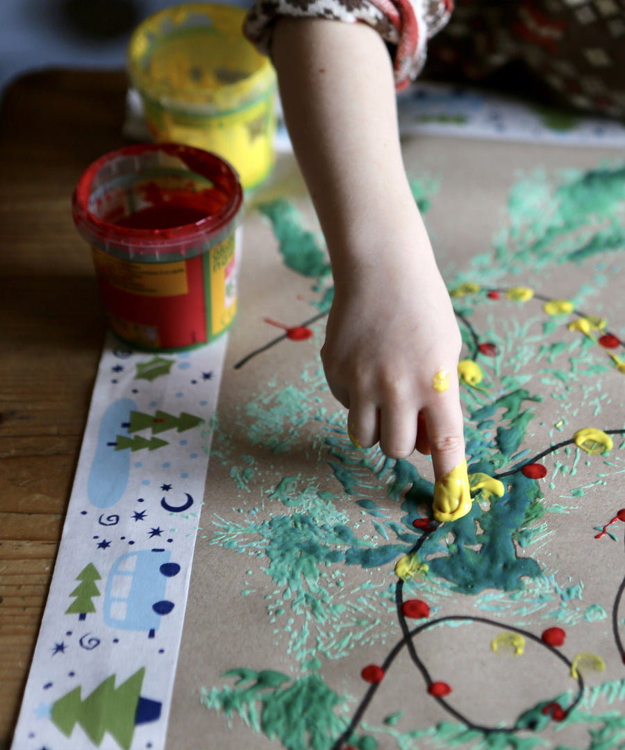 Child creating art with Okonorm finger paints. The child is dotting yellow and red paint to create Christmas tree lights.