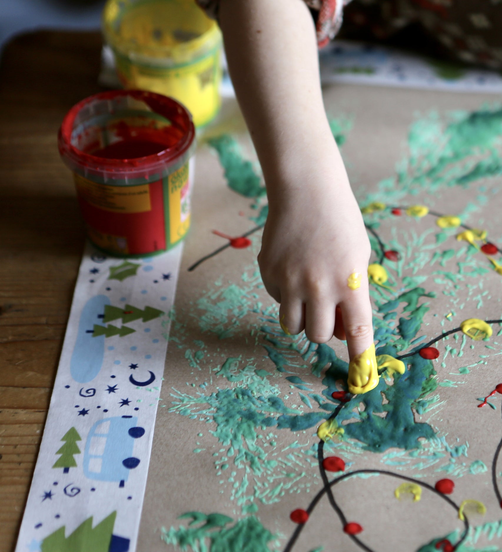 Child creating art with Okonorm finger paints. The child is dotting yellow and red paint to create Christmas tree lights.