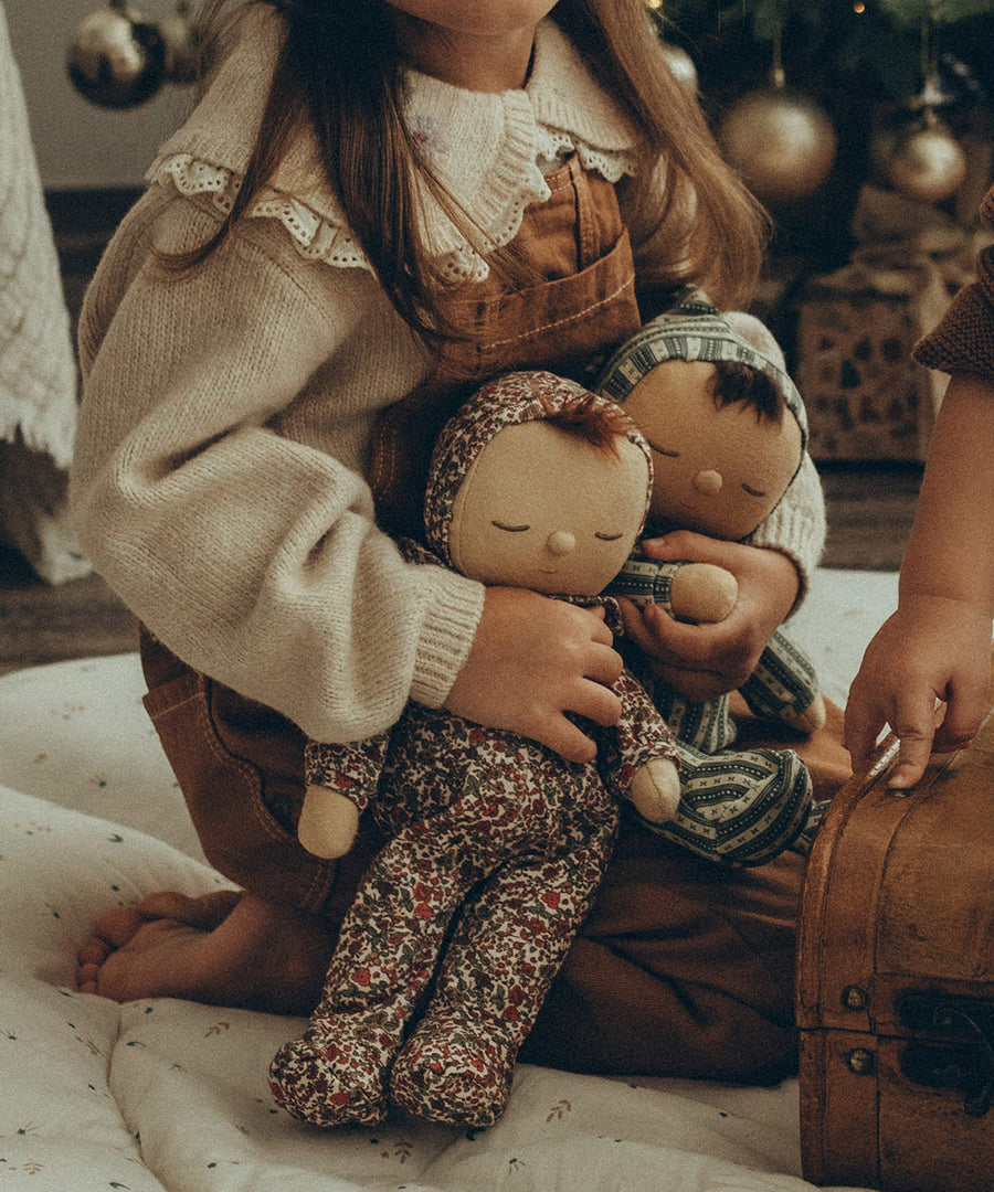 Olli Ella Dozy Dinkum Doll Pudding and Pie being held by a child in their arms. In the background is a Christmas Tree