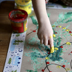 Christmas tape bordering a piece art created by a child using finger paints. The child is adding finishing touches.