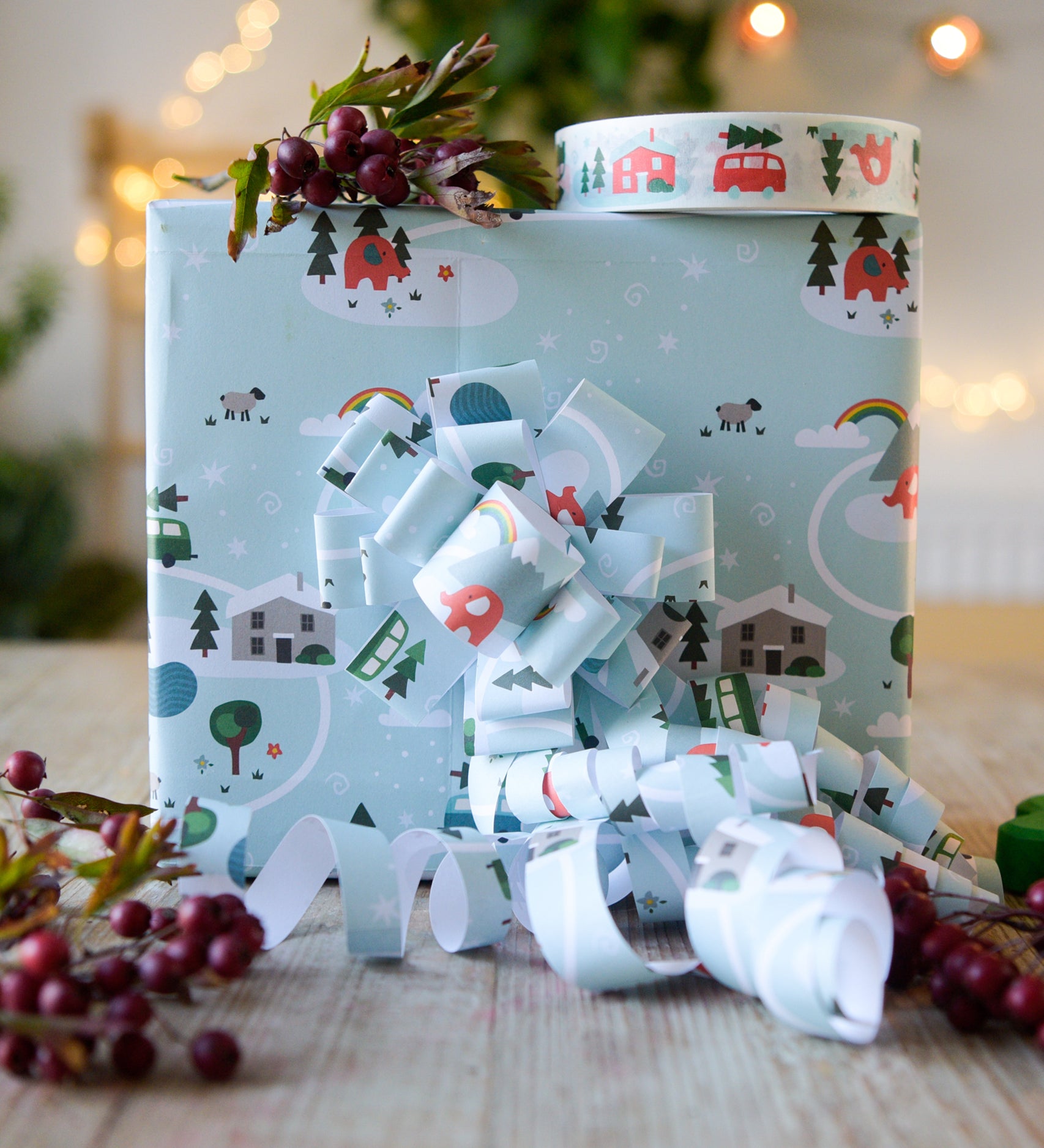 A box on a table wrapped in Babipur Christmas paper. There's a roll of babipur Christmas paper tape on top of the box.