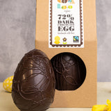 Cocoa Loco organic Fairtrade vegan dark chocolate Easter egg, with chocolate swirl details. Another sits beside it in eco-friendly brown paper packaging, surrounded by bright daffodils and easter eggs.