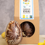 Cocoa Loco organic Fairtrade marbled Easter egg, handmade in the UK with milk, dark, and white chocolate. Another sits beside it in eco-friendly packaging, surrounded by mini eggs and daffodils.