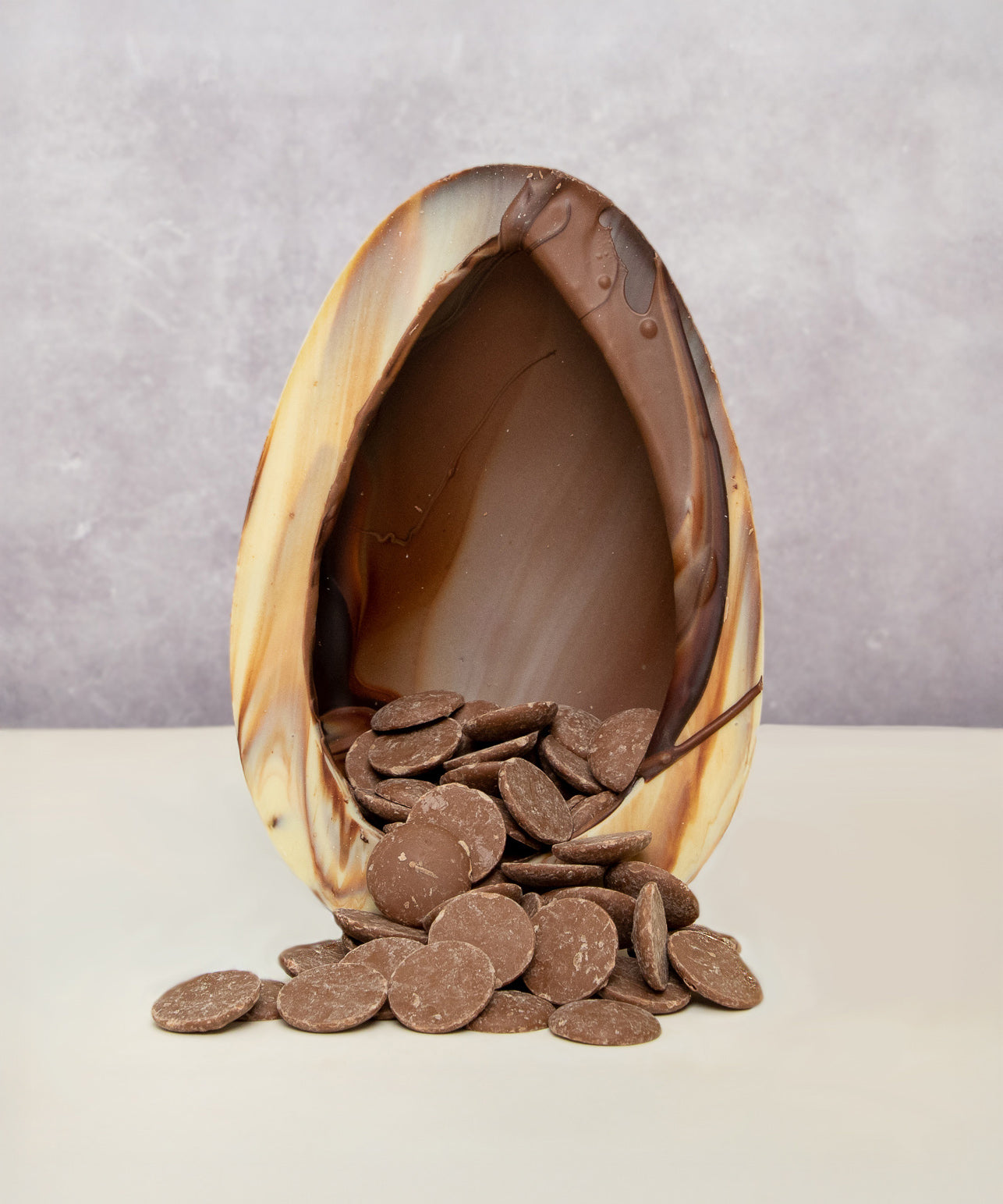 Cocoa Loco organic Fairtrade marbled Easter egg, handmade in the UK, halved to reveal milk chocolate buttons spilling from its centre.