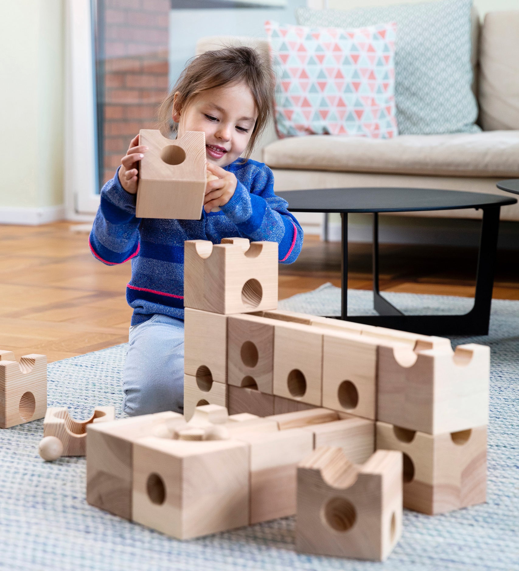 A child playing with the Cuboro XL Wooden Marble Run Set and is holding a block in their hand