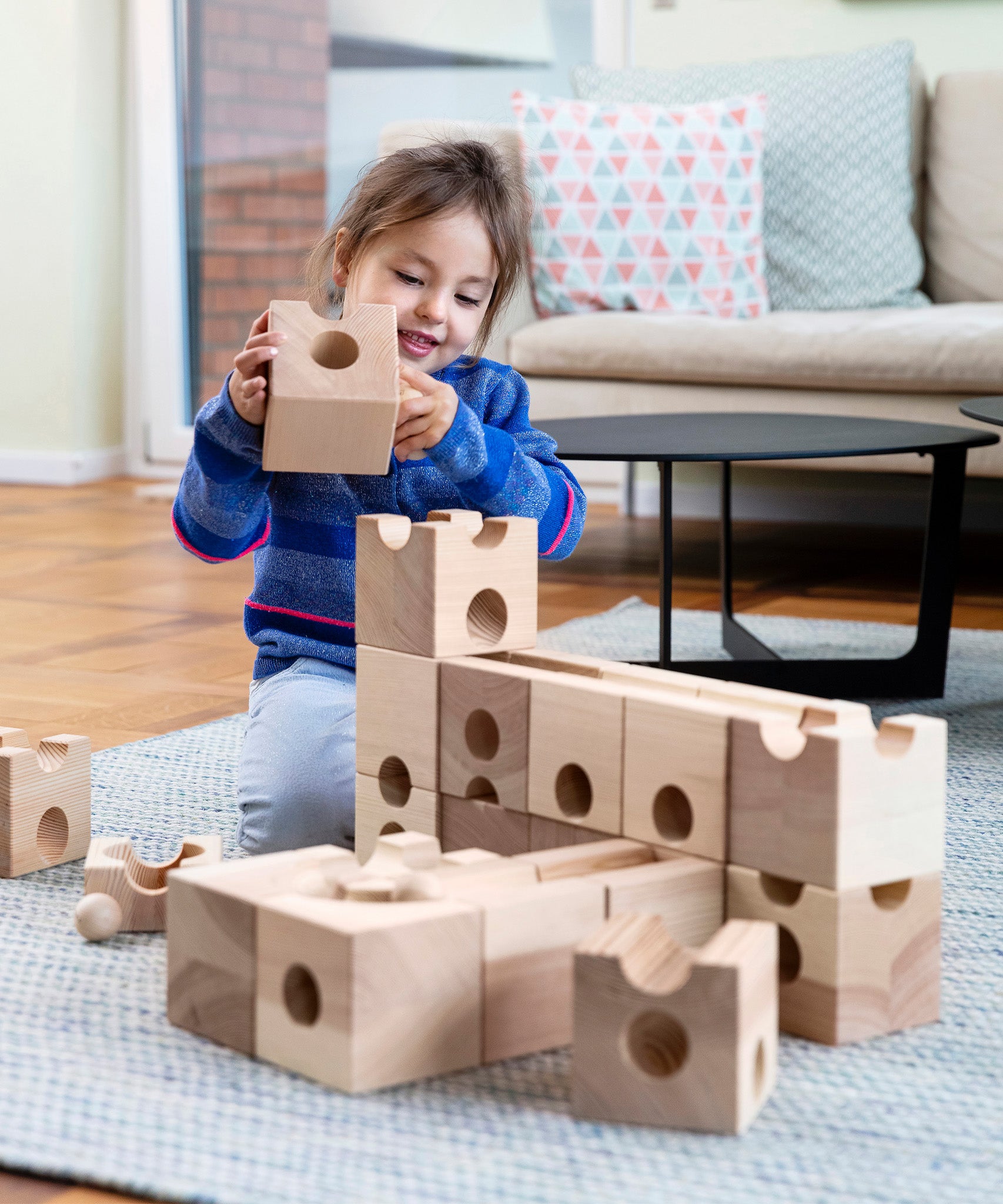 A child playing with the Cuboro XL Wooden Marble Run Set and is holding a block in their hand