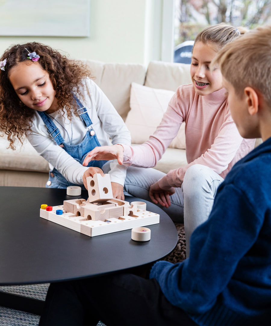 Three children playing with the Cuboro Tricky Ways Board Game on a black table