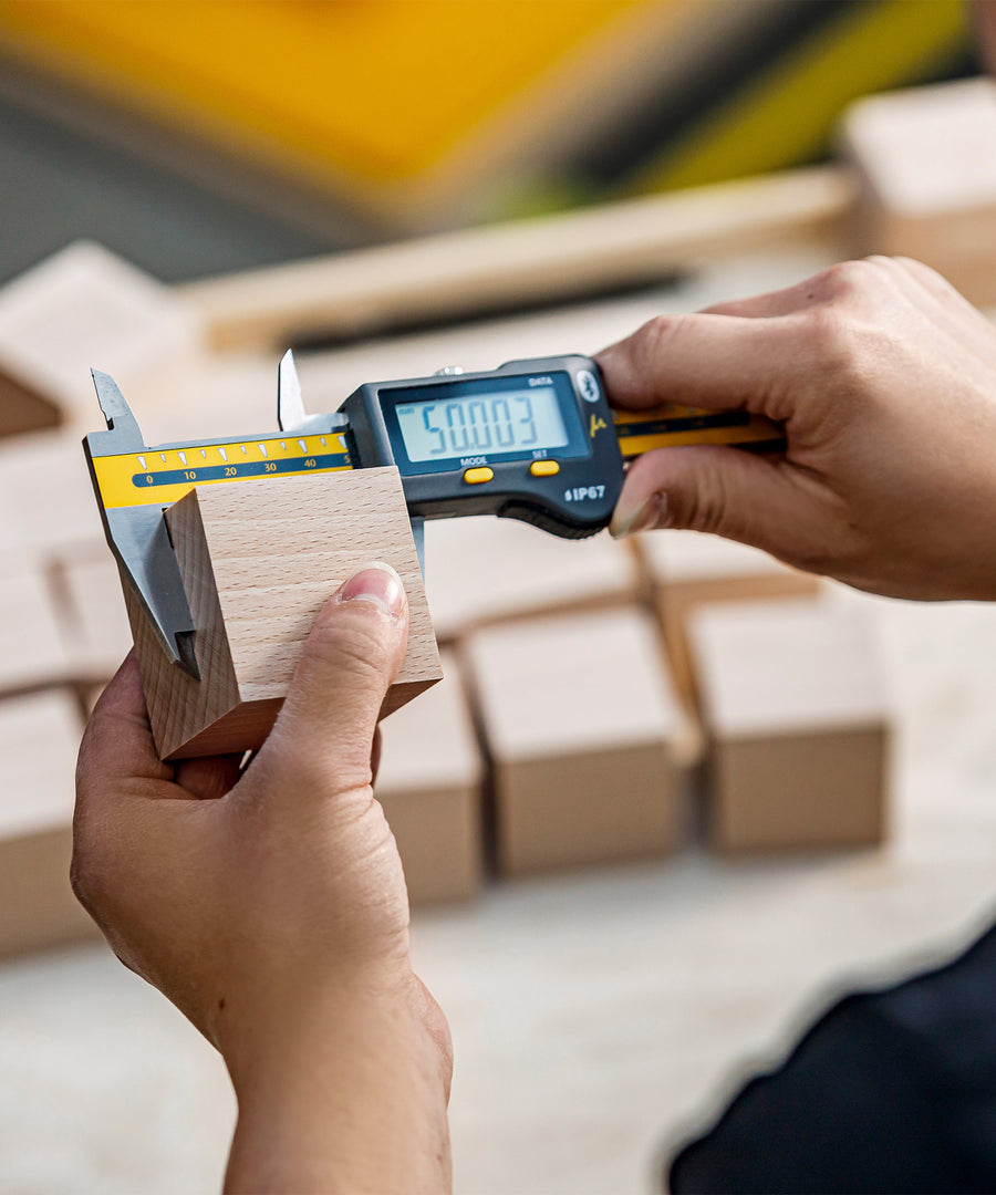 A person measuring a wooden block for a Cuboro block piece, using a handheld electronic measuring tool