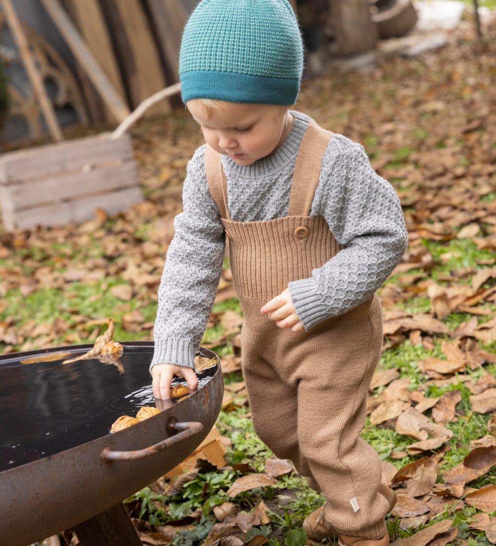 Disana organic merino wool dungarees worn by a toddler playing with leaves 