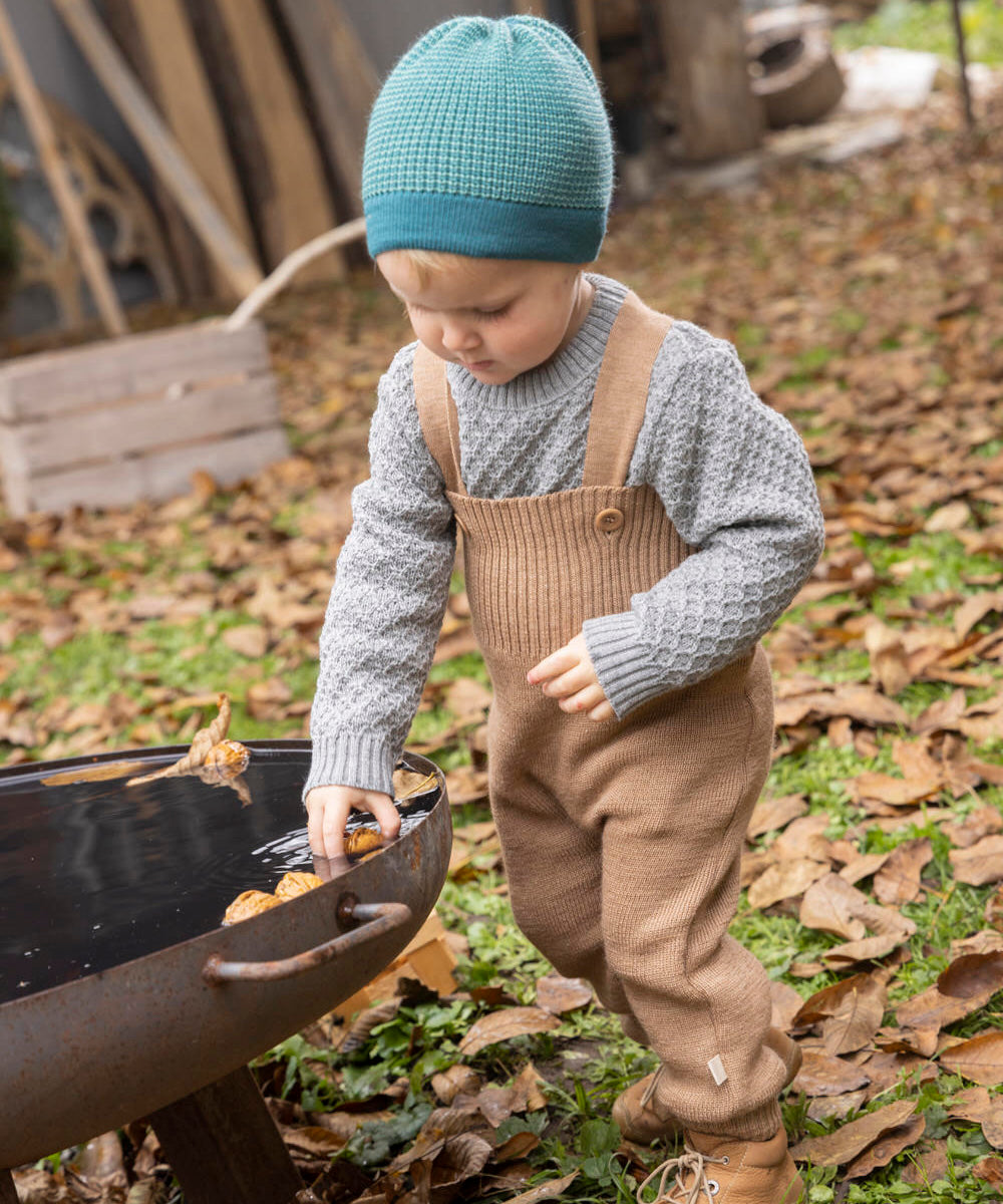 Disana organic merino wool dungarees worn by a toddler playing with leaves 