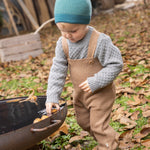 Disana organic merino wool dungarees worn by a toddler playing with leaves 