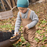 Disana organic merino wool dungarees worn by a toddler playing with leaves 