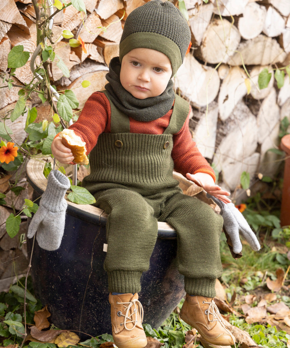 Disana organic merino wool dungarees worn by a toddler sitting on a plant pot