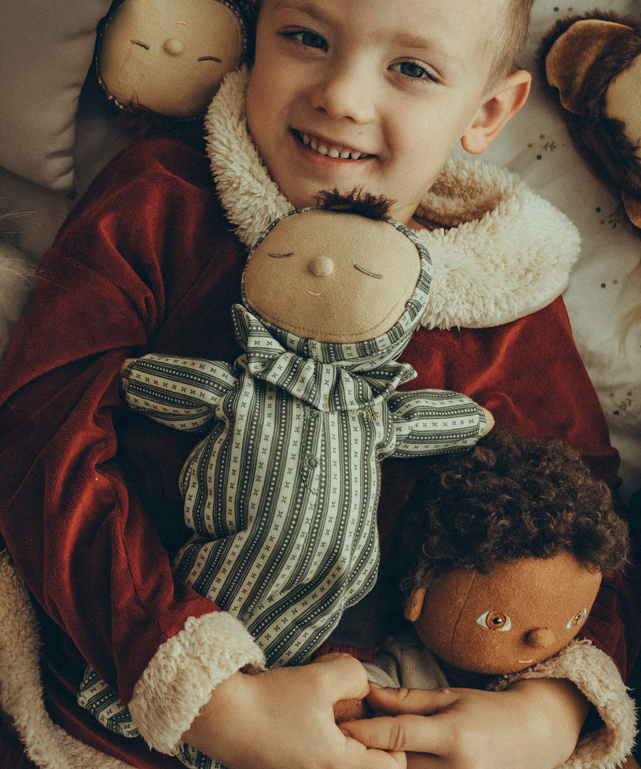 A child holding the Olli Ella Dozy Dinkum Doll Pie - Clover, in their arms with other Olli Ella dolls surrounding them