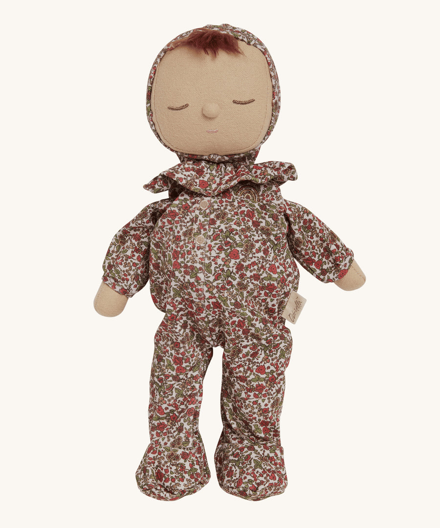 Olli Ella Dozy Dinkum Doll Pudding - Garland, is a soft body doll with a beautiful, vintage style, floral outfit which has a frilly collar and hood, and a tuft of brown hair poking out from underneath. The image is on a cream background.