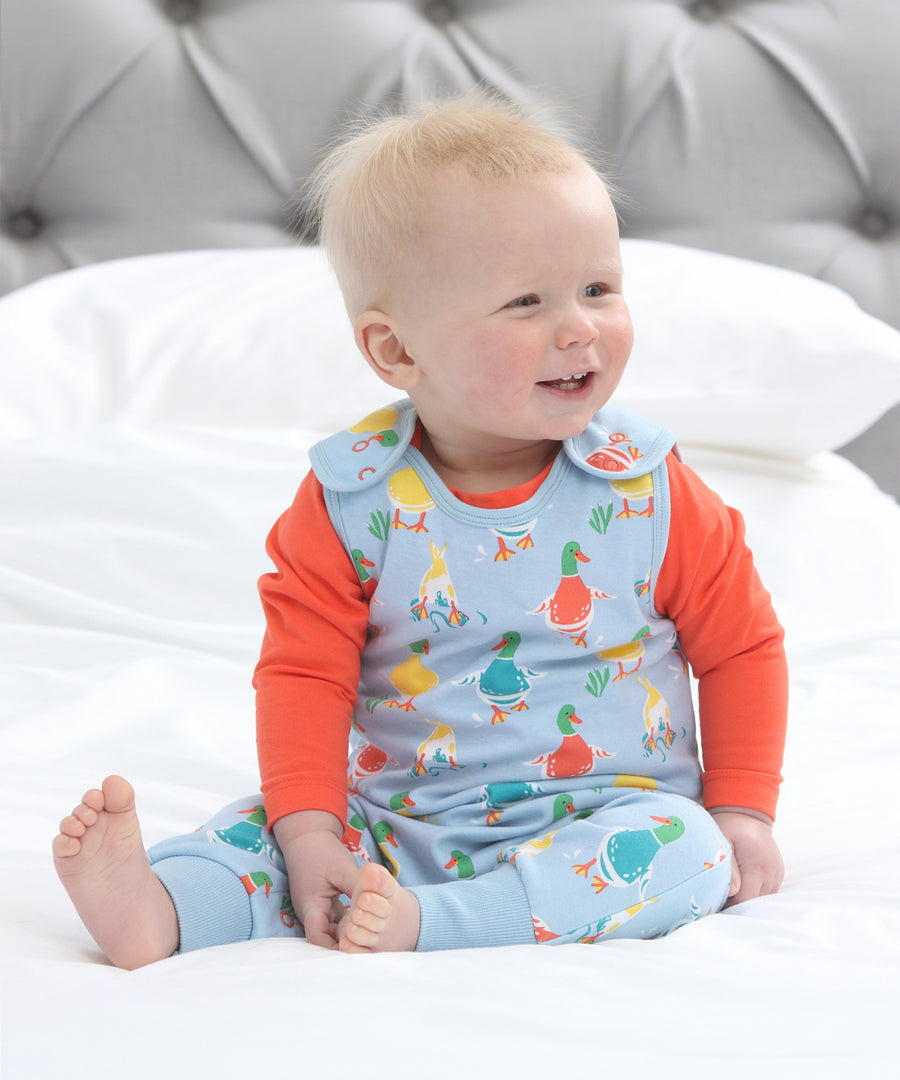 A child wearing the Piccalilly Duck Days Dungarees and an orange top underneath