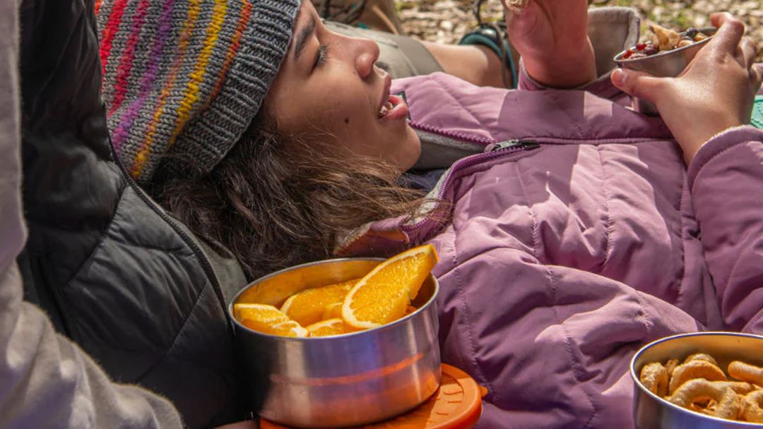 Woman lying down after a hike, enjoying food from an ECOlunchbox