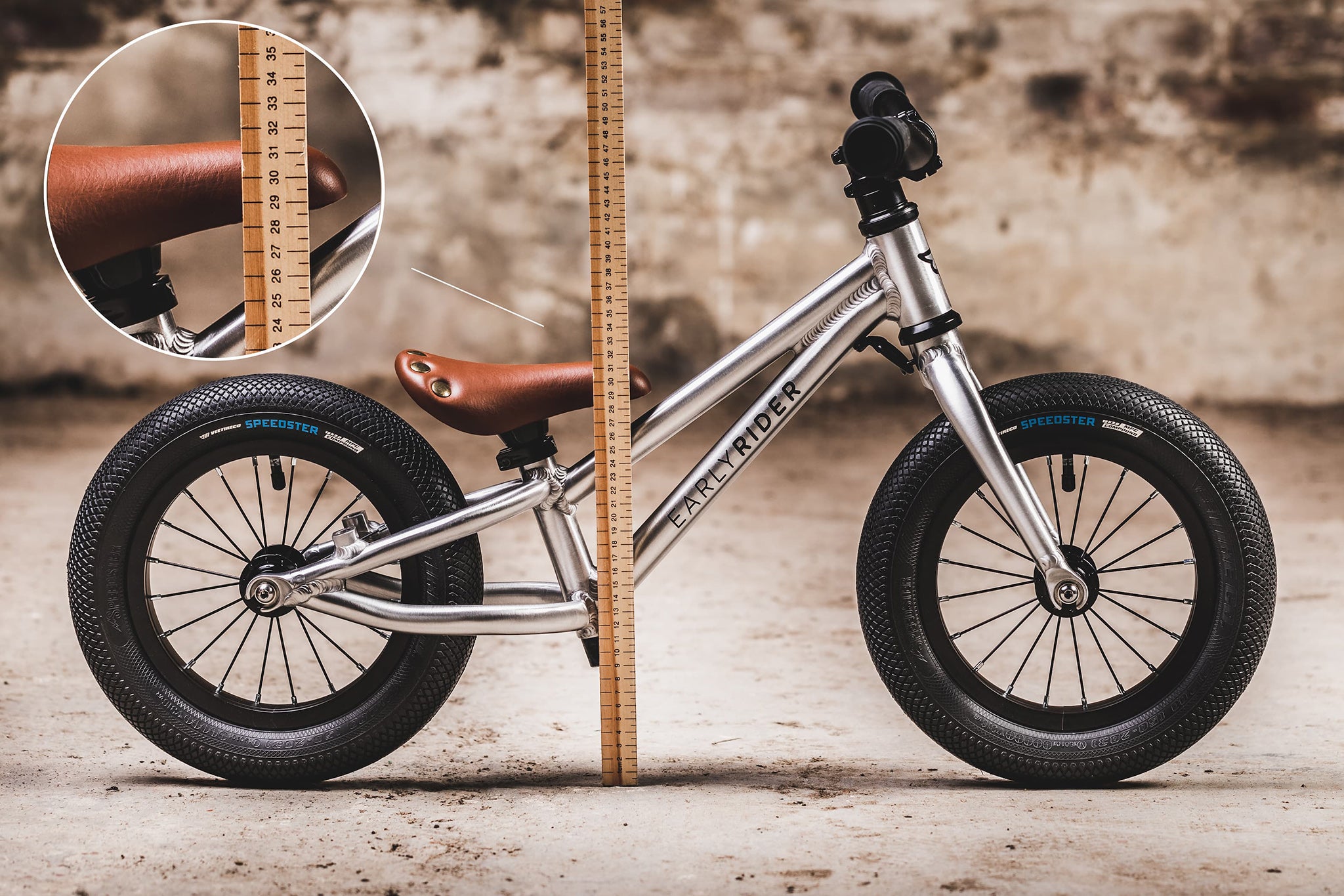 The Early Rider Charger Balance Bike stood behind a light brown measuring ruler, showing the height from the floor to the top of the bike seat