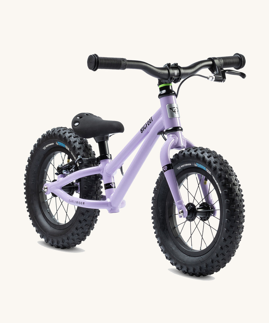 The Early Rider Big Foot Balance Bike - Violet Haze is stood at a slight angle. It has a Violet frame, black wheels, a black seat and black handle bars. The image is on a cream background