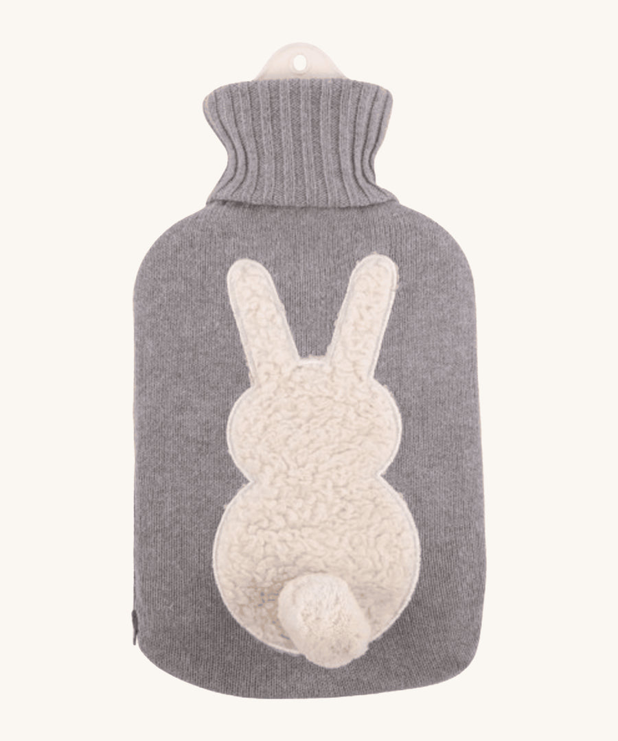 The Ecoliving Natural Rubber Hot Water Bottle - Bunny, has a soft grey knitted cotton cover with a fluffy white bunny silhouette and a cute white cotton tail. The image is on a cream background