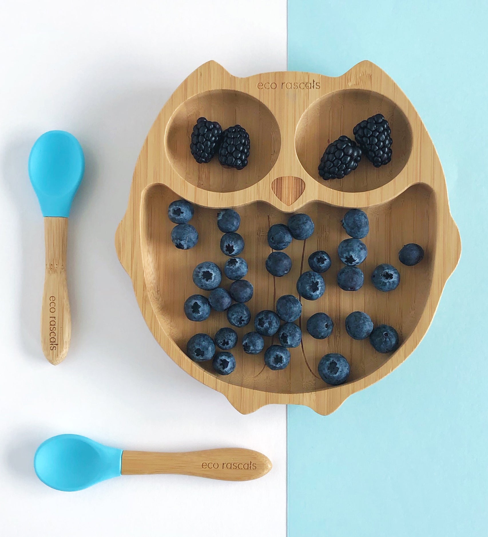 Eco Rascals Owl Bamboo Suction Plate with blackberries and blue berries and two blue silicone and bamboo baby spoons. 