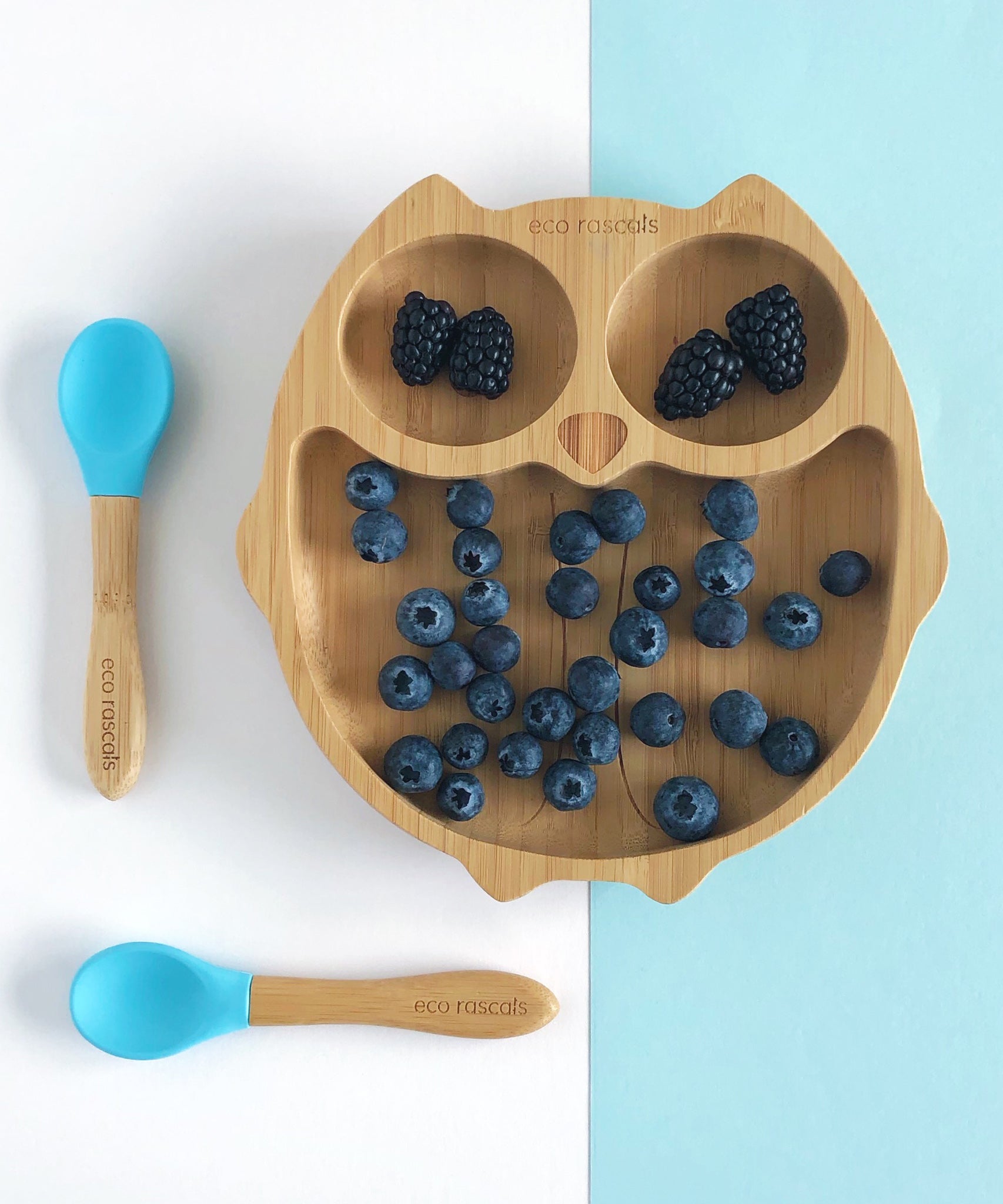 Eco Rascals Owl Bamboo Suction Plate with blackberries and blue berries and two blue silicone and bamboo baby spoons. 