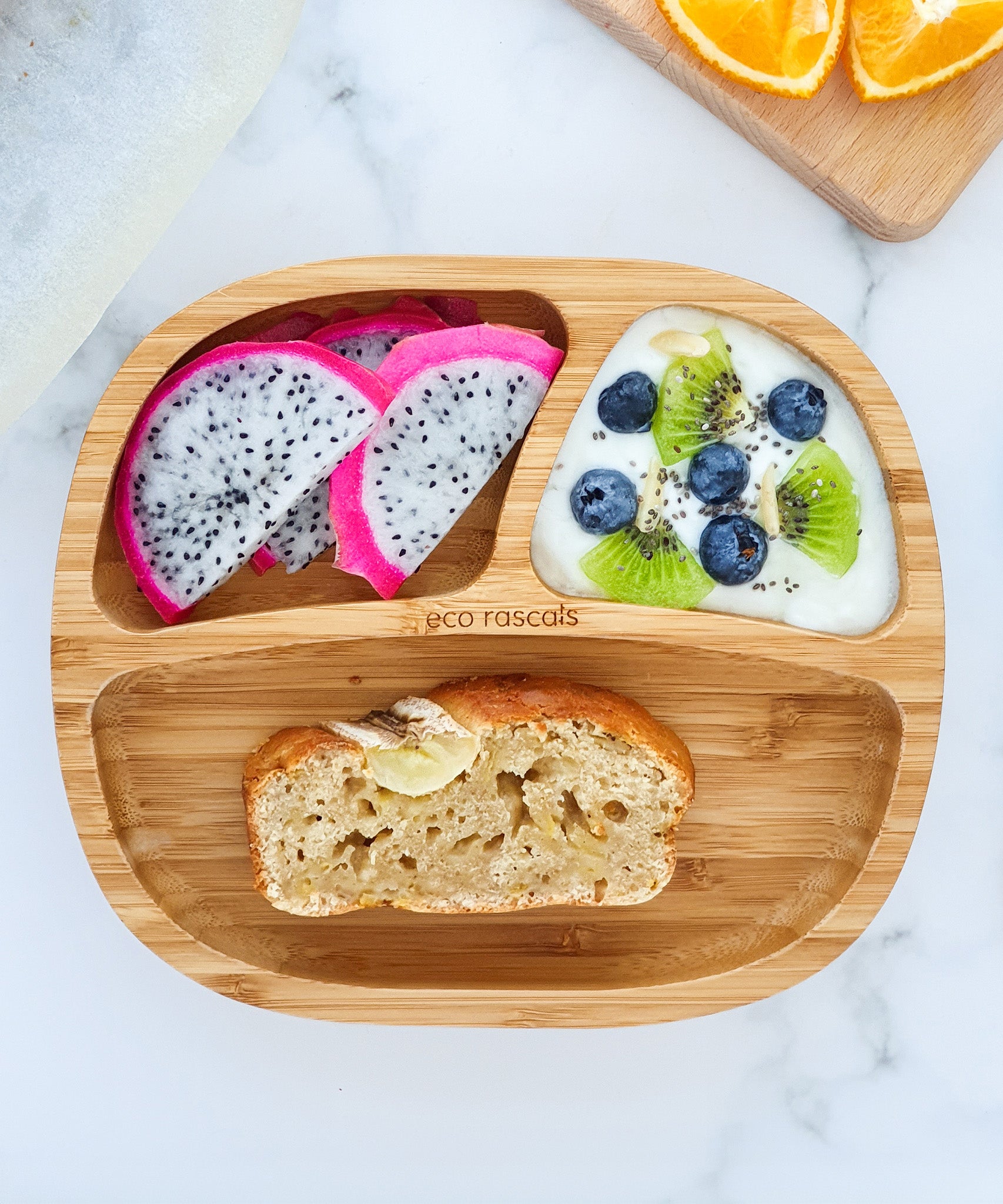 Bamboo baby section plate with banana loaf, dragonfruit slices and yogurt with fresh fruit and berries. 