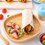 Eco Rascals Rectangle Bamboo Suction Plate, a natural bamboo baby weaning plate with a tortilla wrap and side portion of fruit, with a silicone and bamboo sippy cup. 