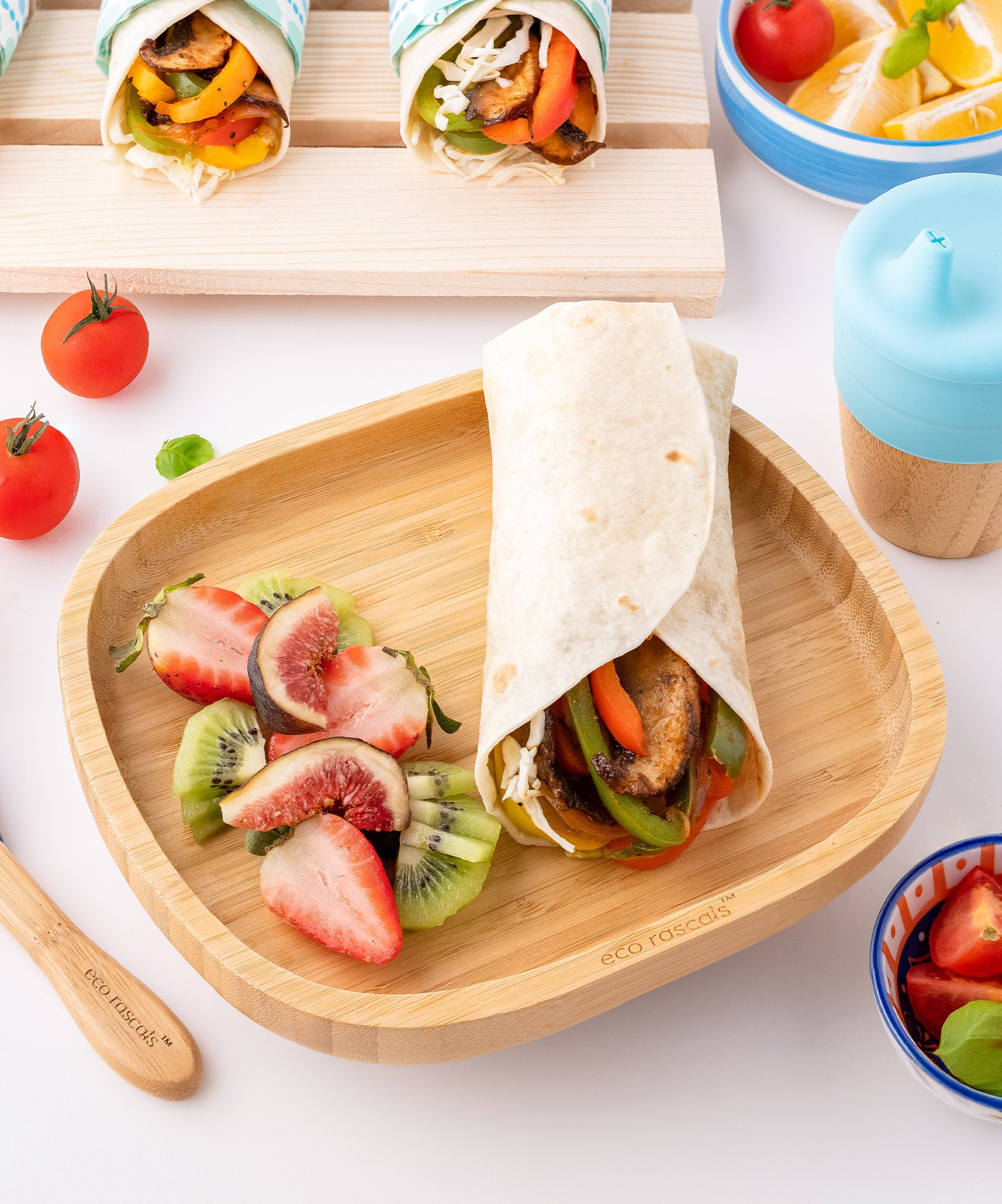 Eco Rascals Rectangle Bamboo Suction Plate, a natural bamboo baby weaning plate with a tortilla wrap and side portion of fruit, with a silicone and bamboo sippy cup. 