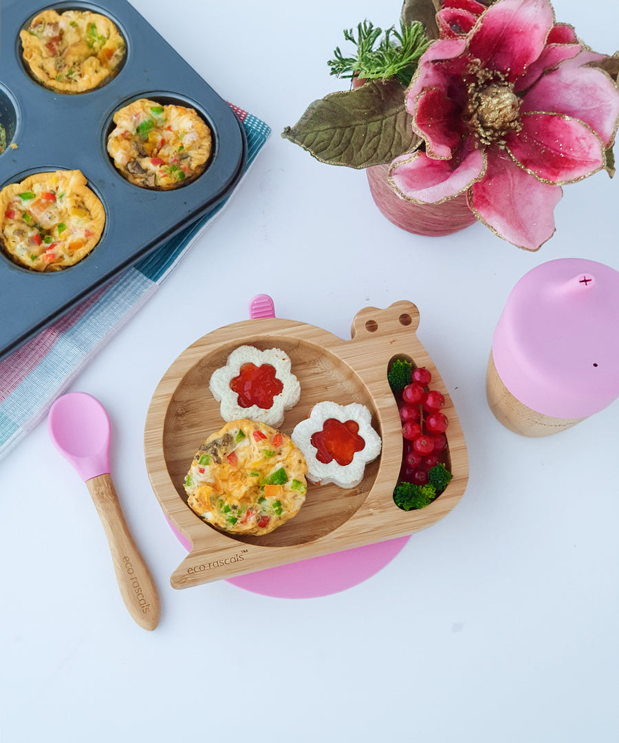 Eco Rascals Snail Plate, Feeder Cup, Bowl & Spoon Gift Set in Pink, with various food items surrounding