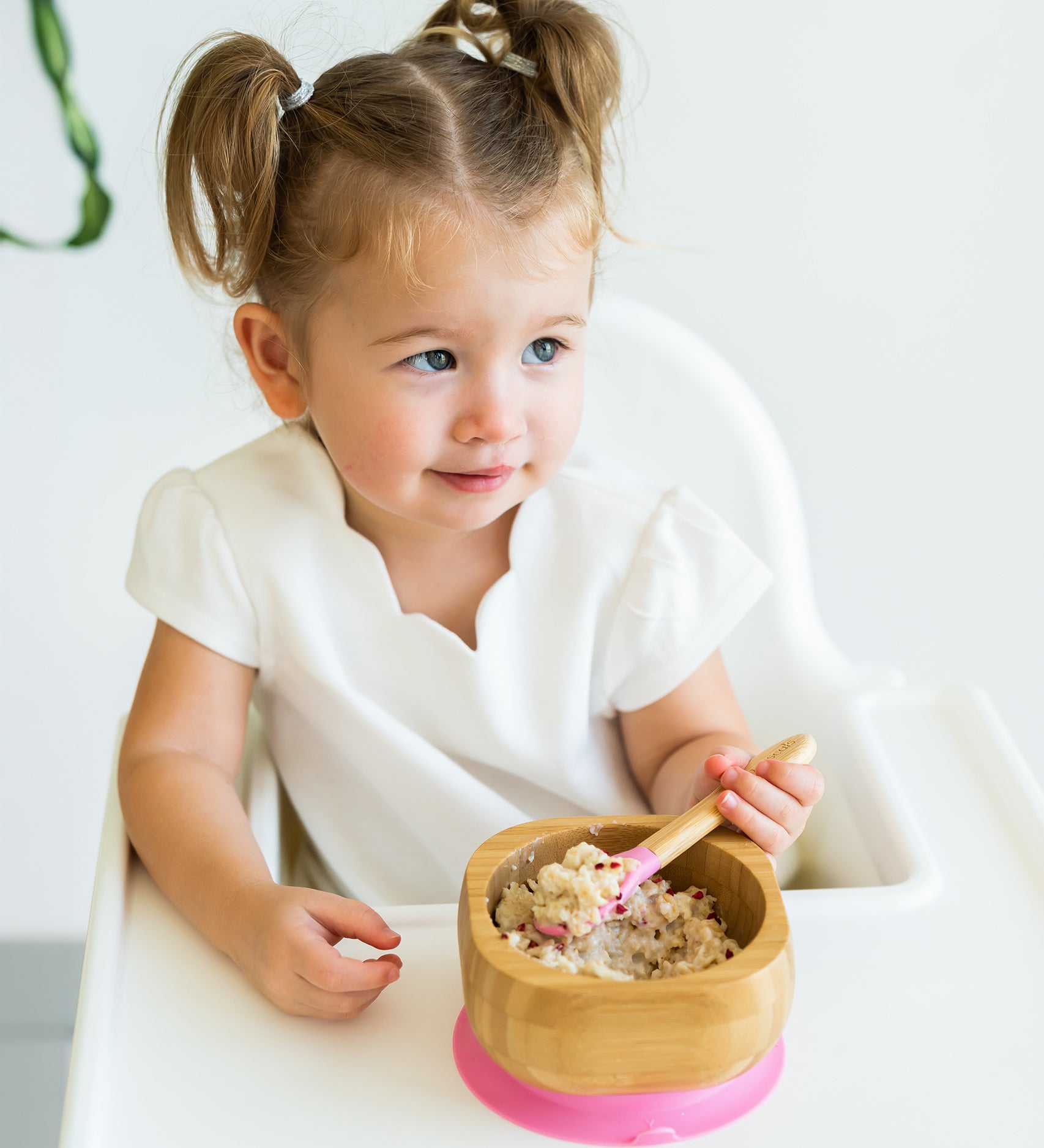 Toddler in a highchair eating porridge from the Eco Rascals Bamboo Bowl & Spoon Weaning Set in pink silicone.