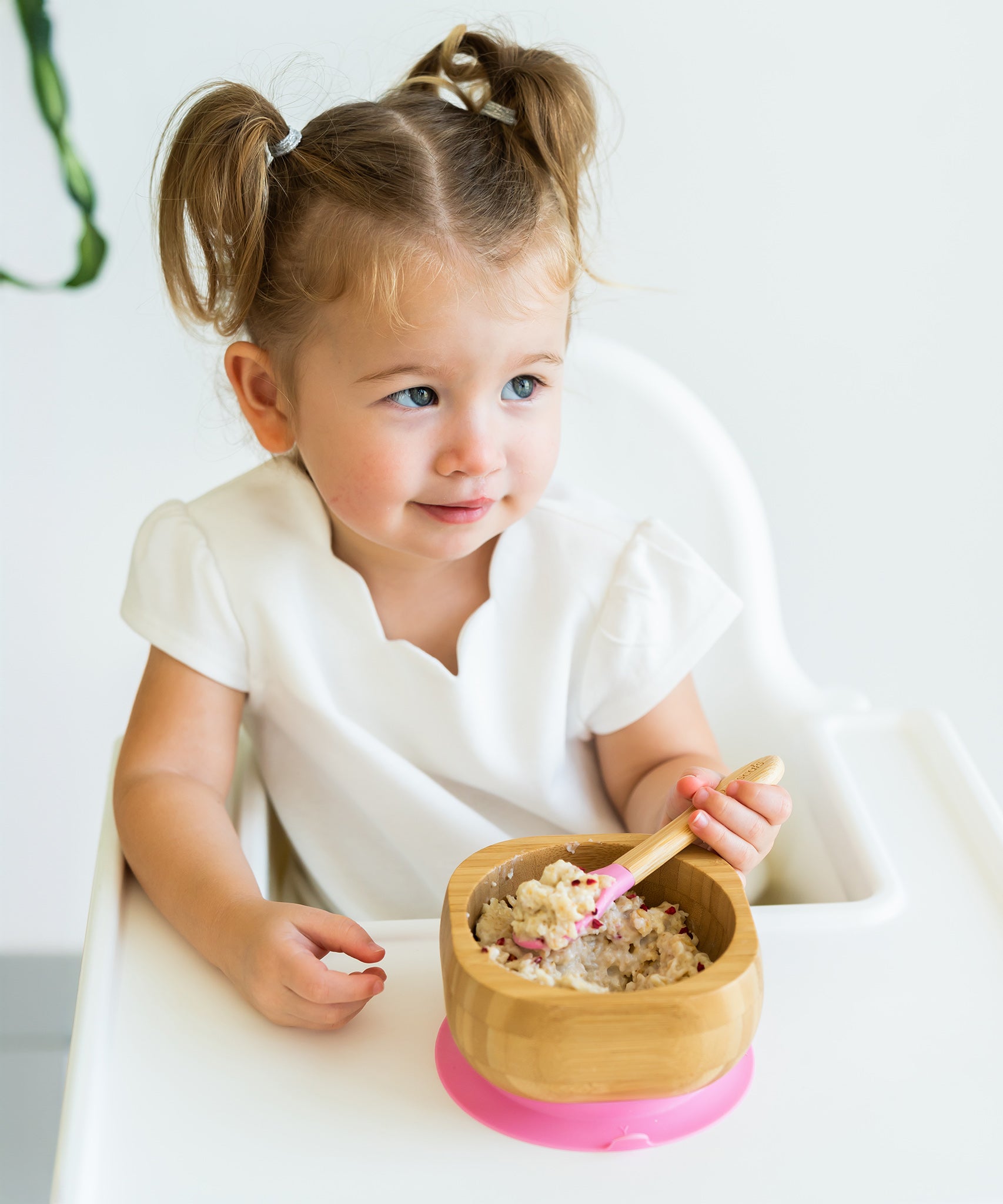 Toddler in a highchair eating porridge from the Eco Rascals Bamboo Bowl & Spoon Weaning Set in pink silicone.