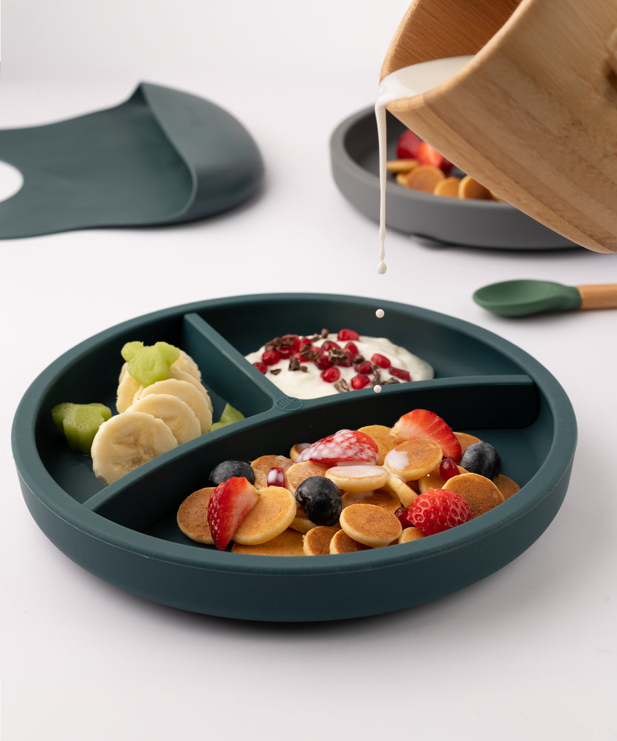 Eco Rascals Silicone Baby Plate in silver with removable divider, someone is pouring milk onto cereal and fruit.  