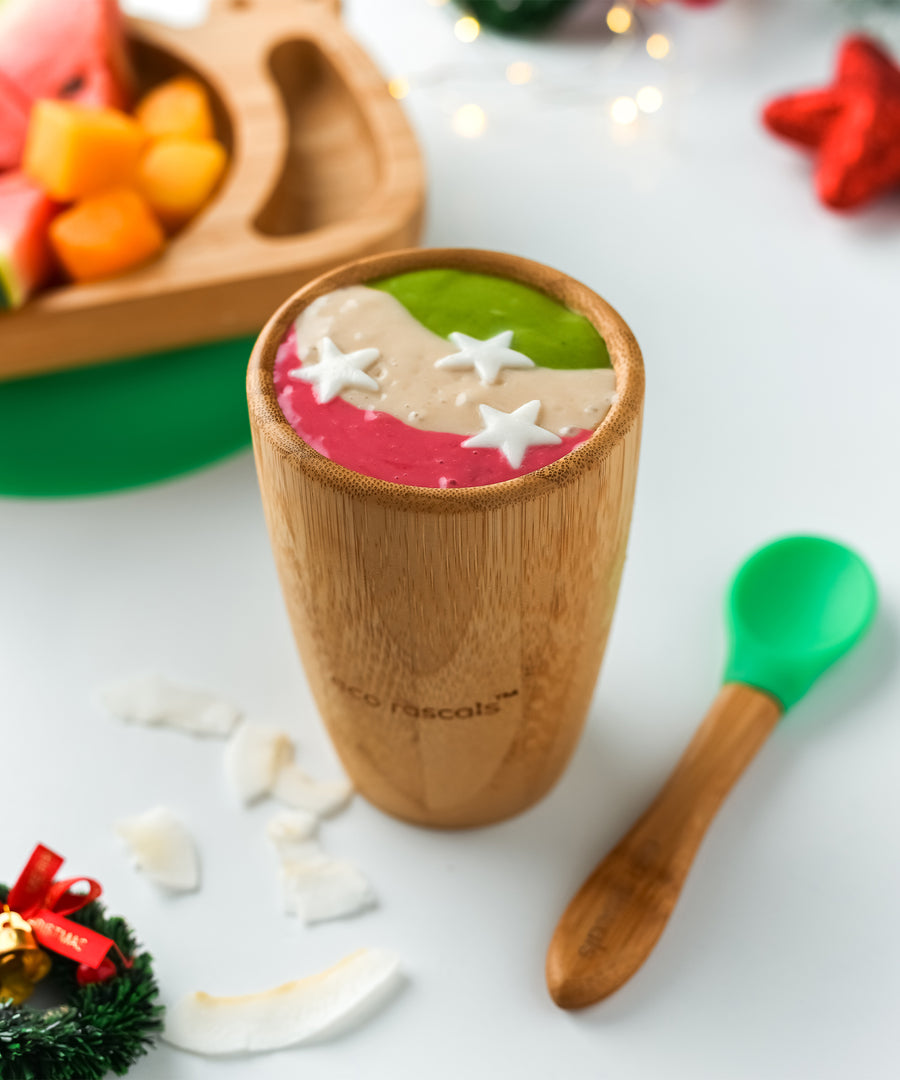 A colourful smoothie in pink, cream and green in a bamboo baby cup with green silicone and bamboo baby spoon. 