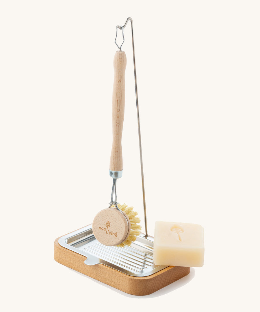 The Ecoliving dish brush holder with an Ecoliving dish soap bar in the soap tray, and an Ecoliving dish brush hanging from the metal hook n the thin pole, on a plain background