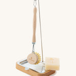 The Ecoliving dish brush holder with an Ecoliving dish soap bar in the soap tray, and an Ecoliving dish brush hanging from the metal hook n the thin pole, on a plain background