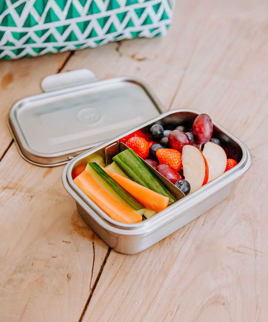 A nice selection of fruit and veg inside the Elephant Box Clip & Seal Lunchbox With Removable Divider - 800ml. The lid is laid behind the lunch box which is on a wooden background